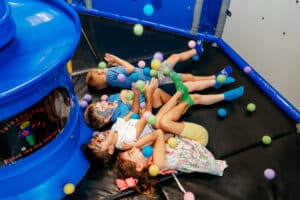 Five-year old boys and girls playing and laughing in a ball pit with balls dropping on them.