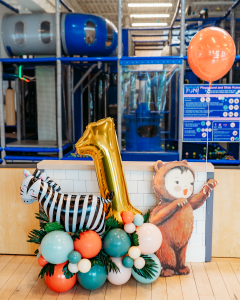 First birthday balloon bouquet with large gold one and zebra balloon with toddler dressed in bear costume holding a red balloon