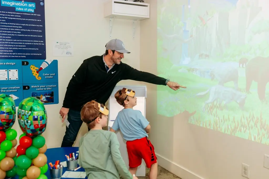 Dad and two young sons watching their animated characters come to life on the Draw Alive screen at the Imagination Art station at Ready Set Fun in Sandy Springs.