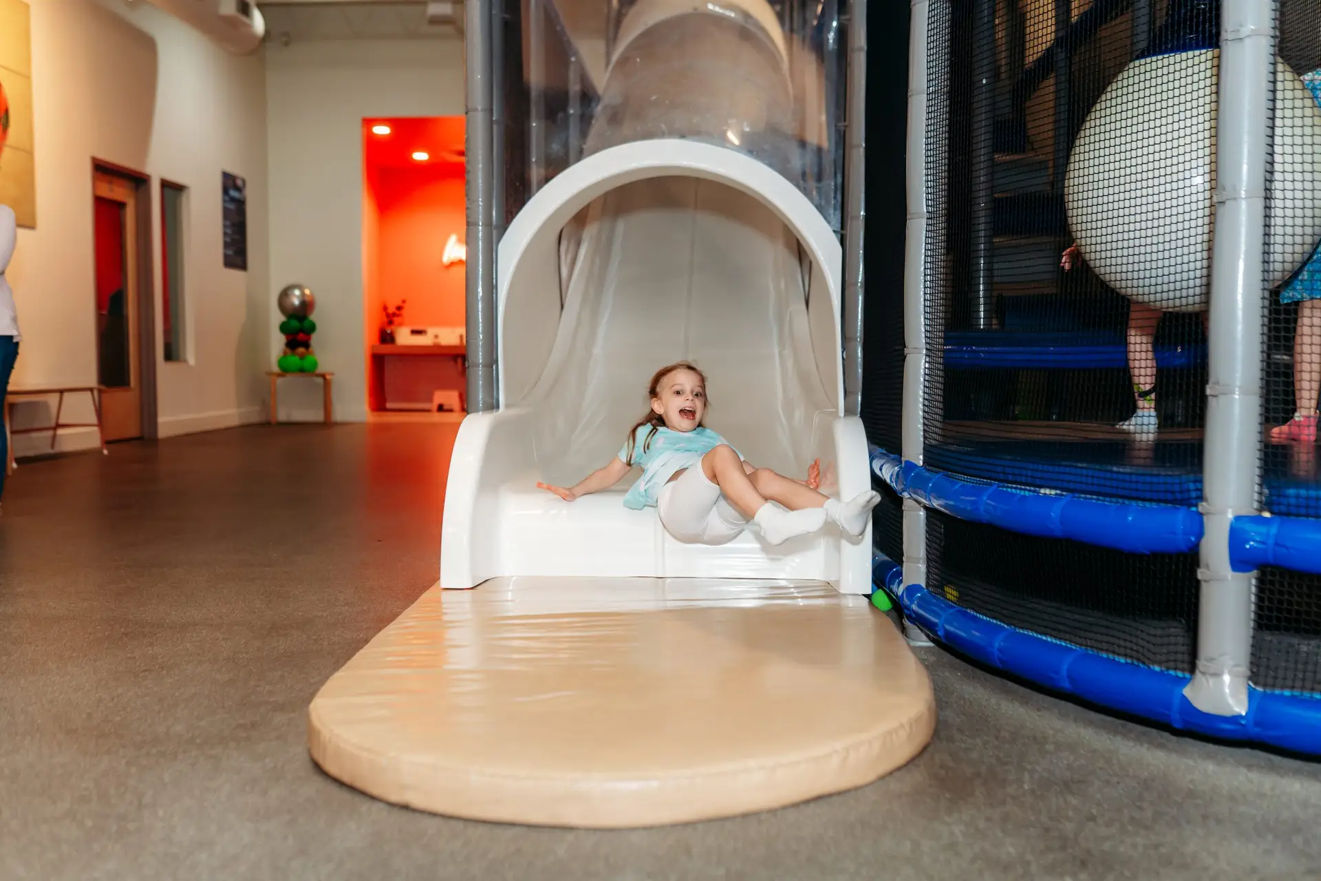 A young girl laughing joyfully as she flies off the big slide at Ready Set FUN indoor playground in Sandy Springs.