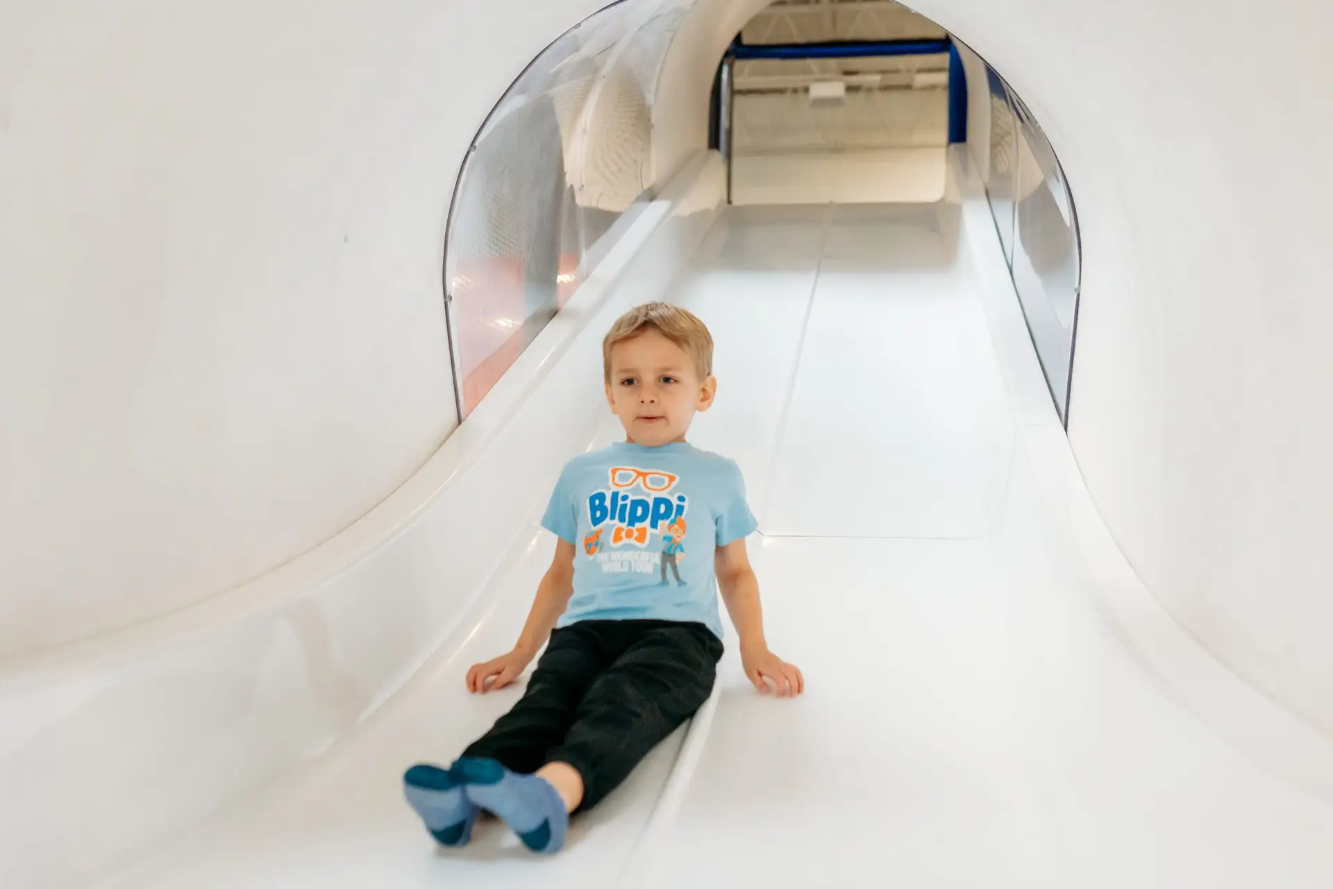A toddler boy riding the big enclosed slide at Ready Set FUN indoor playground in Sandy Springs, Georgia.