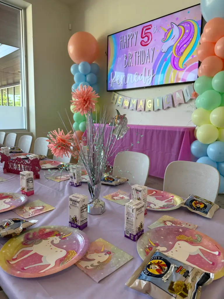 Unicorn themed fourth birthday party private room with rainbow balloon columns, personalized TV sign, and themed table settings at Ready Set Fun in Sandy Springs
